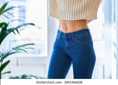 Beautiful slim waist with navel. Skinny figure of a woman in a white warm sweater and jeans. Healthy female body