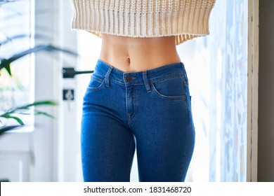 Beautiful slim waist with navel. Skinny figure of a woman in a white warm sweater and jeans. Healthy female body