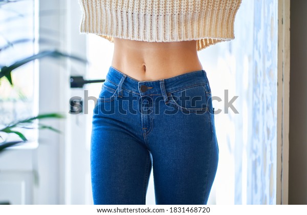 Beautiful slim\
waist with navel. Skinny figure of a woman in a white warm sweater\
and jeans. Healthy female\
body