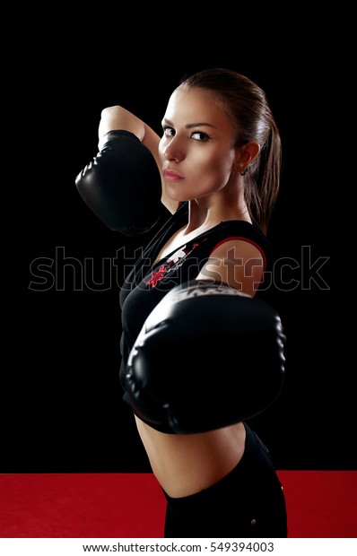 Beautiful slim woman in black top on hand wearing\
boxing gloves standing in the fighter\'s desk on black background.\
The concept of \'strengthening the body and spirit by boxing\'.\
Portrait of the waist