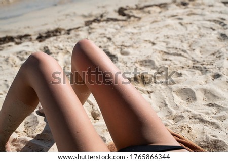Beautiful slim women's legs on the beach. Lower half of the girl body lying on the beach by the sea. Young women's wet and sun-tanned legs on the beach with the sea view.