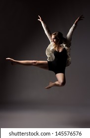 Beautiful Slim Young Female Modern Jazz Contemporary Style Ballet Dancer Wearing A Black Leotard And White Shirt On A Neutral Grey Studio Background