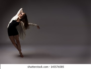 Beautiful Slim Young Female Modern Jazz Contemporary Style Ballet Dancer Wearing A Black Leotard And White Shirt On A Neutral Grey Studio Background