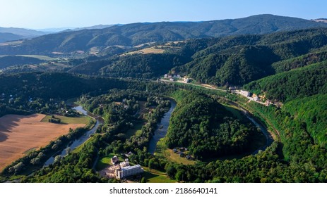 Beautiful Small City At The River Bend In The Mountains. Some Buildngs And Mountains In The Bacground. Aerial Photo, No Clouds, No People.