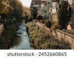 Beautiful small river with clean and clear water front of colorful autumn trees and small old town on the hill agaist nice blue and clouds sky during autumn in Europe