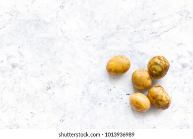 beautiful small rounded whole organic potato with the peel isolated on white marble kitchen top. Horizontal composition. Top view