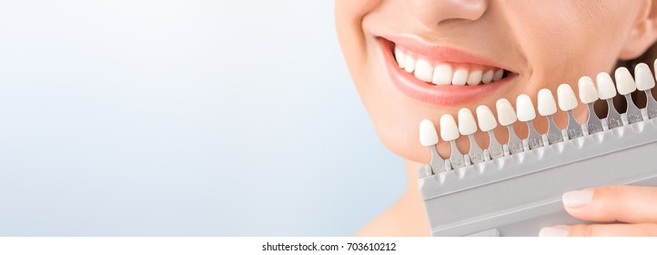 Beautiful smile and white teeth of a young woman. Matching the shades of the implants or the process of teeth whitening. - Shutterstock ID 703610212