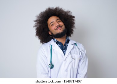 Beautiful Smiling African American Doctor Man With Broad Smile, Shows White Teeth, Wears Medical Uniform, Stands Over Gray Studio Wall Rejoices Having Day Off.