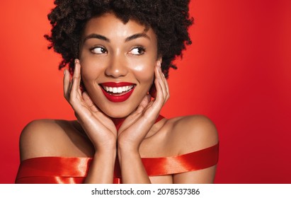 Beautiful Smiling African American Woman With Red Lips, Glowing Naked Body Wrapped In Red Ribbon, Concept Of Skin Care, Winter Holidays And Christmas Gifts