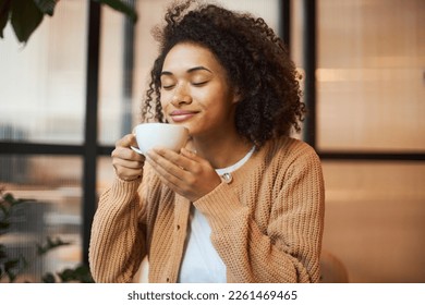 Beautiful smiling African American woman with her eyes closed, enjoying her morning coffee in modern cafe. Coffee break concept - Powered by Shutterstock