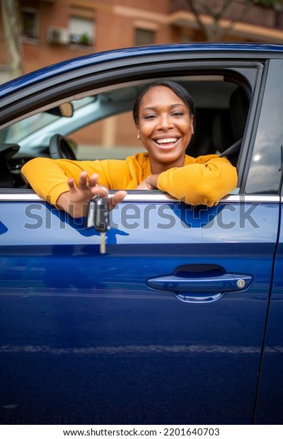 Beautiful smiling african american woman sitting\
in her new car and showing the\
keys