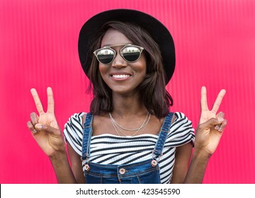 Beautiful smiling african woman in a black hat over colorful pink background. Fashion portrait stylish woman in sunglasses outdoor.