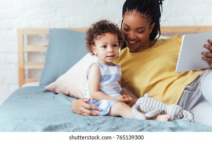 Beautiful smiling African woman enjoying time at home with her baby daughter and holding tablet.