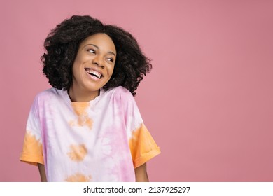 Beautiful Smiling African Woman Looking Away Isolated On Pink Background, Copy Space. Happy Curly Haired Fashion Model Wearing Stylish Tie Dye T Shirt Posing For Pictures In Studio 