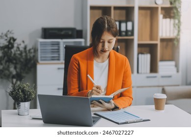 Beautiful smiling Asian businesswoman holding a coffee cup while taking notes at office.