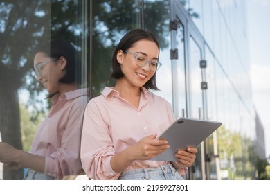 Beautiful Smiling Asian Businesswoman Wearing Stylish Eyeglasses Holding Digital Tablet Working Online Standing On Street.  Successful Business. Happy Female Shopping Online Using Modern Technology