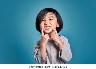 Beautiful Smiling Asian Little Kid Show His Teeth. Empty Space In Studio Shot Isolated On Colorful Blue Background. Education Concept For School.