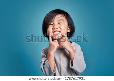 Beautiful smiling asian little kid show his teeth. Empty space in studio shot isolated on colorful blue background. Education concept for school.