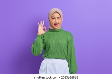 Beautiful Smiling Asian Woman In Green Sweater Showing Okay Gesture Demonstrates Symbol Of Approval Isolated Over Purple Background