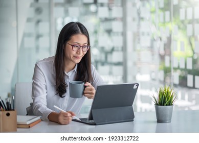 Beautiful Smiling Asian Woman Is Happy To Work Using A Tablet And Drinking Coffee At The Office.