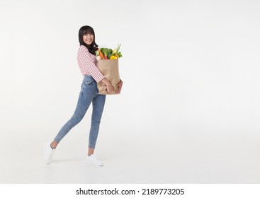 Beautiful smiling Asian woman holding shopping bag full of groceries and looking to copy space aside isolated on white background. - Powered by Shutterstock