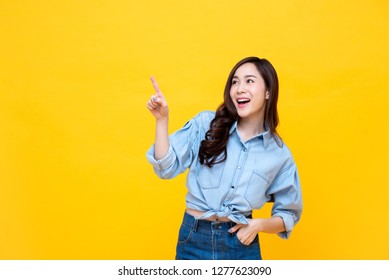 Beautiful smiling Asian woman pointing hand to empty space aside studio shot isolated on colorful yellow background