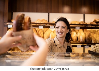 Beautiful smiling bakery worker selling pastry to the customer in bakery shop.
