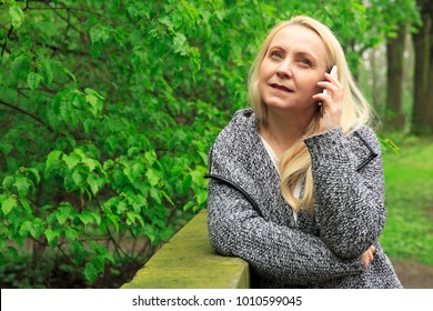 Beautiful Smiling Blond Woman 45 Years Old In City Park Talks On A Phone.