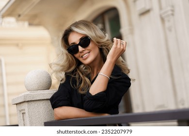 Beautiful smiling blond woman in elegant luxury sunglasses posing on the street. European background. Perfect wavy hairs. - Shutterstock ID 2352207979