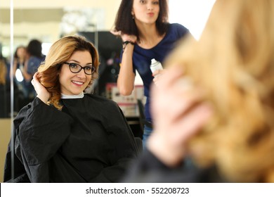 Beautiful Smiling Blonde Woman At Hairdresser Checking And Fixing New Curly Hairdo With Hand. Keratin Restoration, Latest Trend, Fresh Idea, Haircut Picking, Shorten Tips, Instrument Store Concept