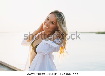 Beautiful smiling blonde young woman in white shirt on pier on sunset