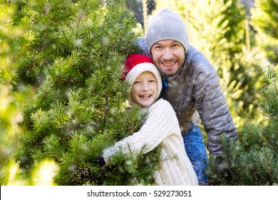 beautiful smiling boy in santa's hat, sweater and mittens and his father choosing christmas tree at market or farm at winter, holiday concept