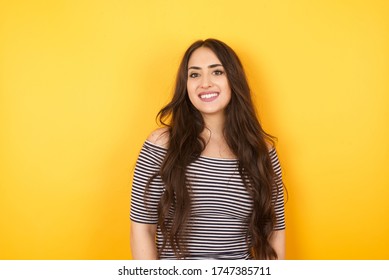 Beautiful smiling brunette female with broad smile and long hair, shows white teeth, wears casual t shirt, stands over yellow studio wall rejoices having day off. Woman standing indoors. - Powered by Shutterstock