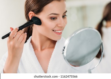 Beautiful Smiling Brunette Girl In Bathrobe Applying Powder Bronzer With Brush