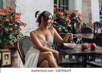 Beautiful smiling brunette girl having lunch in a street cafe, sitting at a table and eating Italian pasta. Advertising, commercial design.