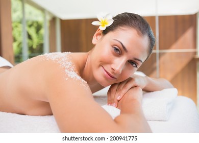 Beautiful smiling brunette lying on massage table with salt scrub on back in the health spa