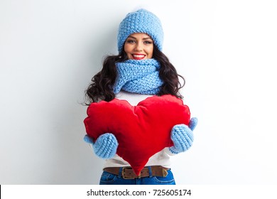 Beautiful Smiling Brunette Woman In Winter Hat And Scarf Holding A Red Heart Pillow