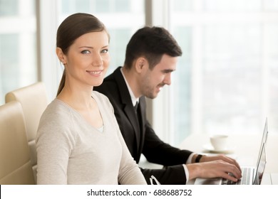 Beautiful smiling businesswoman built successful career posing at workplace with laptop near colleague, ambitious lady looking at camera in office, powerful women in business leadership, portrait