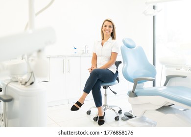 Beautiful Smiling Caucasian Female Dentist Sitting With Legs Crossed On Chair