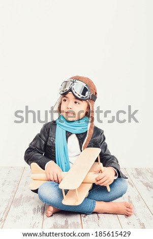Beautiful smiling child (kid, girl) in helmet on a white background playing with a plane. Vintage pilot (aviator) concept