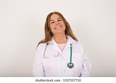 Beautiful Smiling Doctor Female With Broad Smile, Shows White Teeth, Wears Medical Uniform, Stands Over White Studio Wall Rejoices Having Day Off.