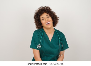 Beautiful Smiling Doctor Female With Broad Smile, Shows White Teeth, Wears Medical Uniform, Stands Over Gray Studio Wall Rejoices Having Day Off.