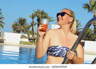 Beautiful smiling European blonde model dressed bikini looking to the side posing with drink in a pool. Summer time, beauty, holiday, recreation, travel and explore the world concept. - Powered by Shutterstock