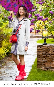 Beautiful Smiling European Woman Dressed Up In A Raincoat With An Umbrella In The Park. Style And Fashion