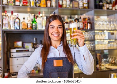 Beautiful smiling female Bartender serving a draft beer at the bar counter , shelves full of bottles with alcohol on the background - Powered by Shutterstock