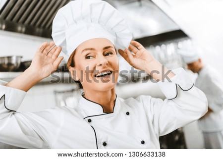 beautiful smiling female chef adjusting cap in restaurant kitchen