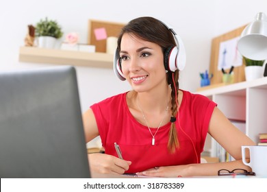 Beautiful Smiling Female Student Using Online Education Service. Young Woman Looking In Laptop Display Watching Training Course And Listening It With Headphones. Modern Study Technology Concept