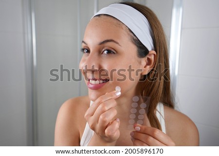 Beautiful smiling girl applying acne treatment anti-pickel patch on a pimple in bathroom