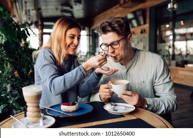 Beautiful smiling girl feeds her handsome boyfriend, eating tasty cake and drinking coffee, spending time together at cafe. - Powered by Shutterstock