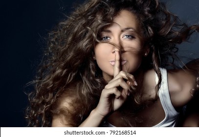 Beautiful Smiling Girl With Flying Curly Hair With A Finger At Her Lips. Keep Silence. The Secret Concept